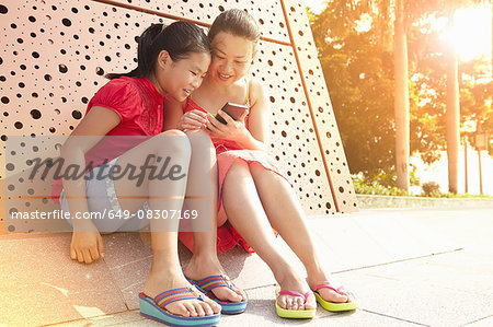 Mid adult woman and daughter reading smartphone texts, Zhuhai, Guangdong, China