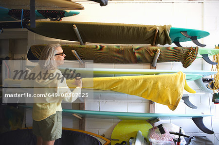 Senior woman taking surfboard from shelf