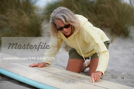 Senior woman on beach, waxing surfboard