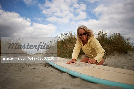 Senior woman on beach, waxing surfboard