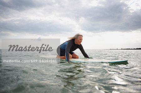 Senior woman on surfboard in sea, paddleboarding