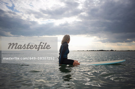 Senior woman sitting on surfboard in sea, rear view