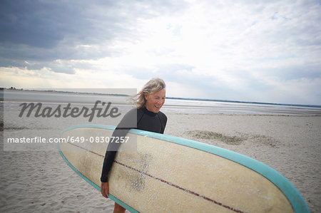 Senior woman walking from sea, carrying surboard