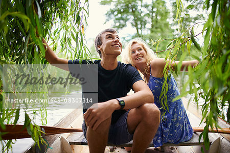 Young couple touching willow tree foliage from rowing boat on rural river