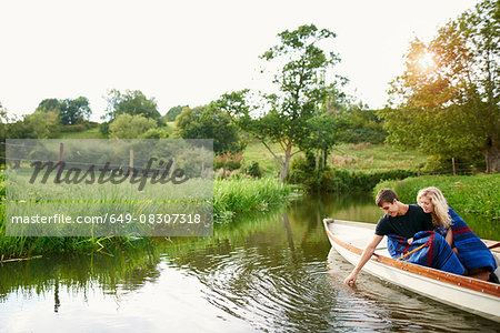 Young man with girlfriend touching water from river  rowing boat