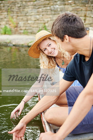 Young couple touching water from rowing boat on rural river