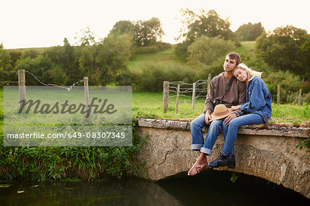 Romantic young couple sitting on river footbridge