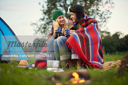 Young camping couple sitting by campfire with cup of tea