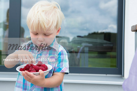 Male toddler on patio eating a bowl of raspberries