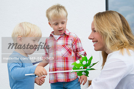 Mother and two young sons playing with pinwheel on patio