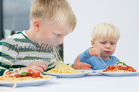 Boy and toddler brother eating spaghetti on patio