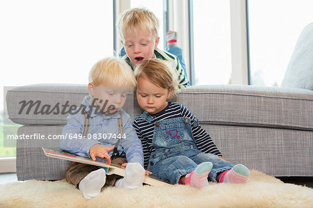 Boy and two toddlers reading childrens book on living room floor