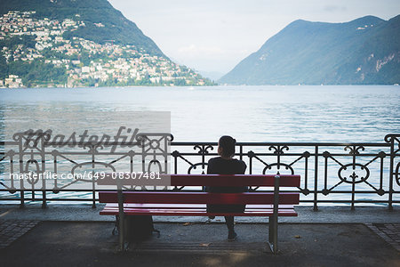 Rear view of silhouetted woman on park bench looking out at Lake Lugano, Switzerland