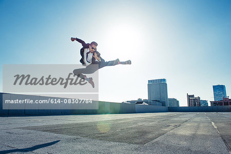 Businessman doing flying kick on roof terrace, Los Angeles, California, USA