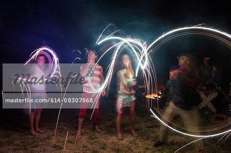 Four adult friends celebrating with sparklers in darkness on Independence Day, USA