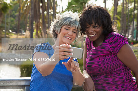 Mature female friends in park, looking at smartphone, laughing