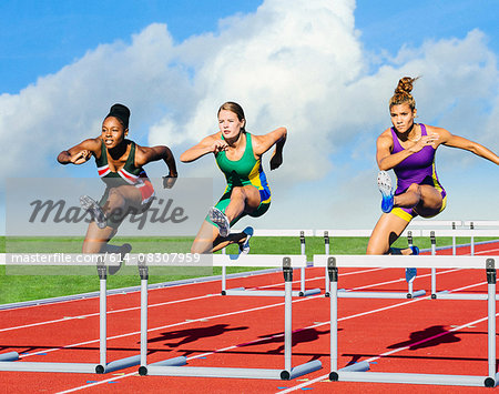 Runners jumping over hurdle on track