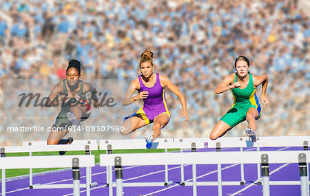 Runners jumping over hurdle on track