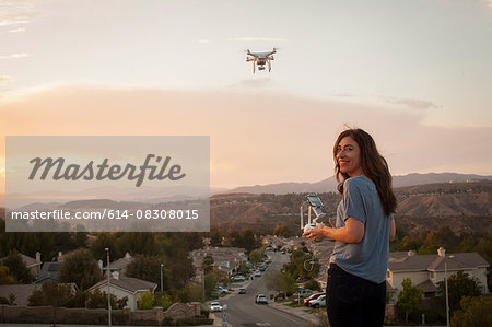Female commercial operator flying drone above housing development, looking over shoulder at camera, Santa Clarita, California, USA