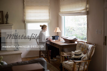 Blond woman sitting at a desk by a window, looking at photographs.