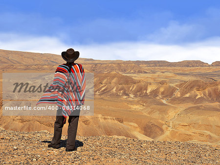 Men in a poncho in the desert. Blue sky and yellow desert.