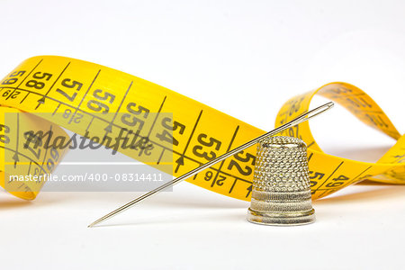 Sewing items (needle, thimble and meter tape) in a white background.