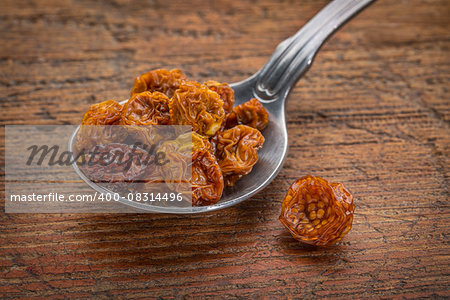 dried goldenberries on a  tablespoon against rustic scratched wood