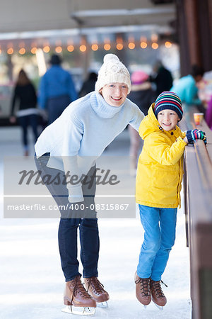 young mother teaching her positive son ice skating, enjoying winter time at outdoor skating rink together