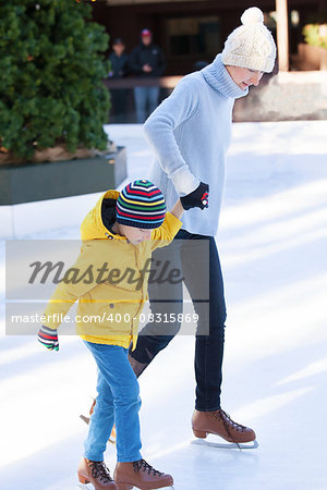 young mother teaching her positive son ice skating, enjoying winter time at outdoor skating rink together