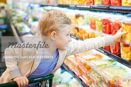 positive 6-year old boy buying healthy fruits at supermarket or grocery store helping his parents