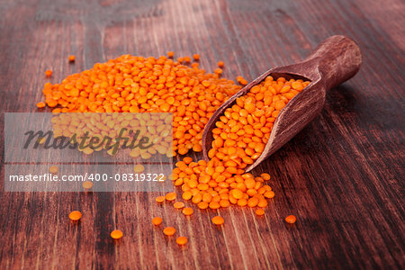 Red lentils on wooden spoon on dark wooden background. Healthy legume eating.