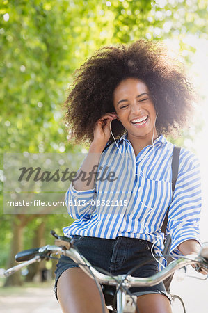 Enthusiastic woman with afro riding bicycle listening to music on headphones