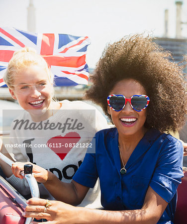 Portrait enthusiastic friends with British flag riding double-decker bus