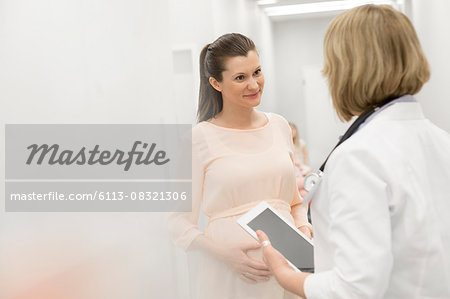 Doctor with digital tablet talking to pregnant patient in clinic corridor