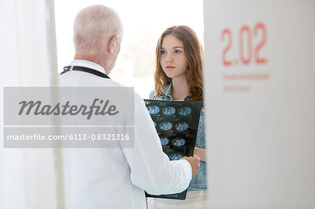 Doctor discussing x-rays with serious teenage patient in examination room