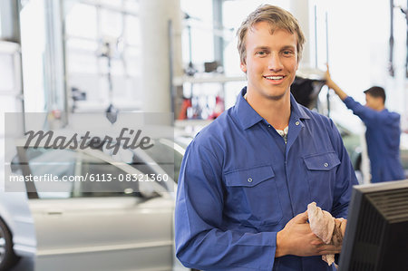 Portrait smiling mechanic at computer in auto repair shop