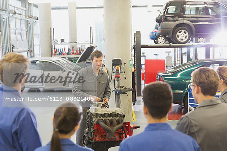 Mechanic explaining car engine to students in auto repair shop