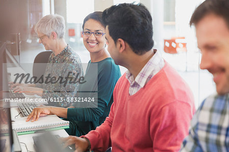 Smiling students talking at computers in adult education classroom