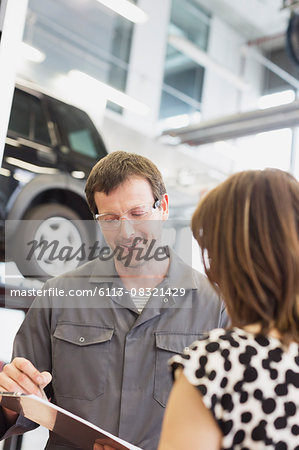 Mechanic with clipboard talking to customer in auto repair shop