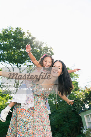 Portrait carefree mother piggybacking daughter with arms outstretched