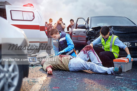 Rescue workers tending to bloody car accident victim in road