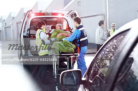 Rescue workers tending to car accident victim on stretcher at back of ambulance