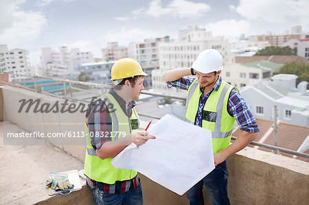 Construction worker and engineer reviewing blueprints at highrise construction site