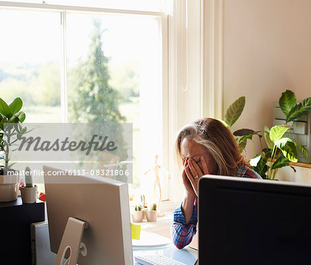 Tired woman with head in hands at computer in home office