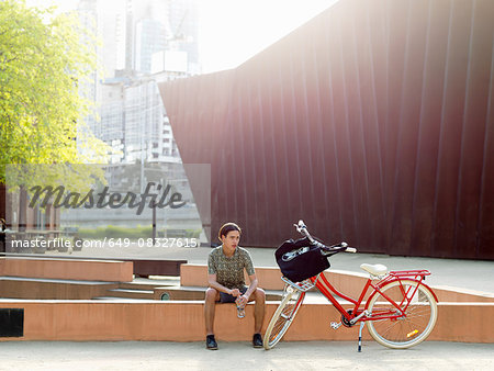 Young man taking break beside bicycle, Southbank, Melbourne, Australia