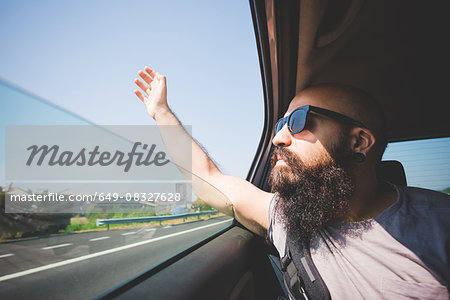 Bearded man sticking hand out of car window on highway, Garda, Italy