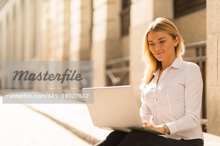Businesswoman using laptop on kerb, London, UK