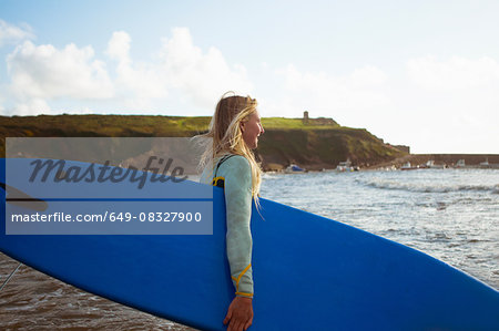 Female surfer walking toward sea, carrying surfboard