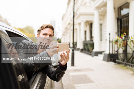 Young man taking photographs from car window, London, England, UK