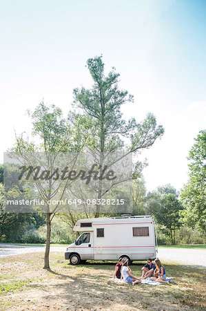 Group of young adults sitting on picnic blanket , relaxing, camper van in background